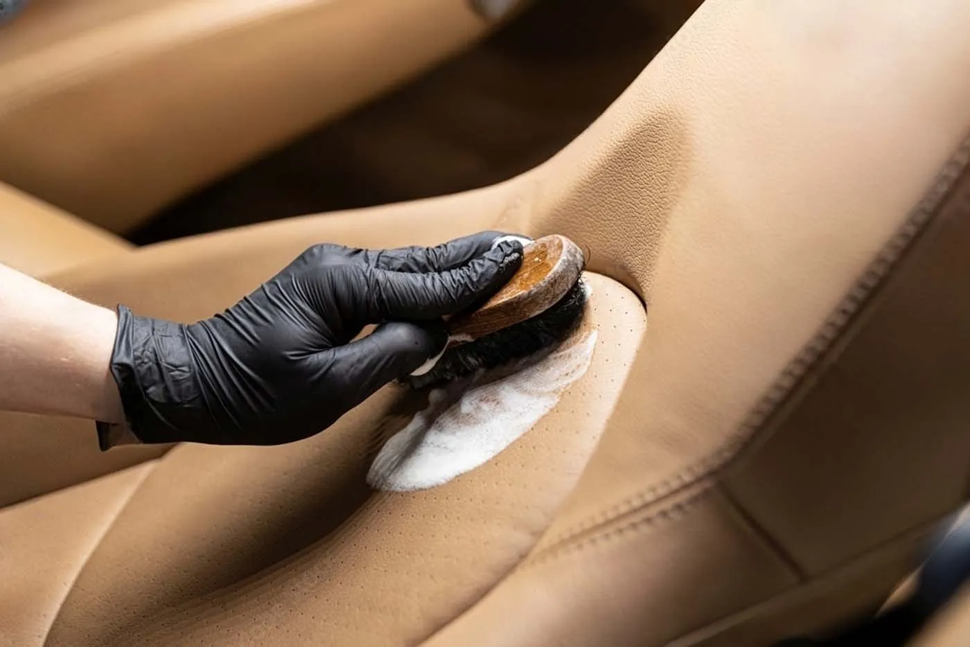 Hand with black glove cleaning leather seat with a brush